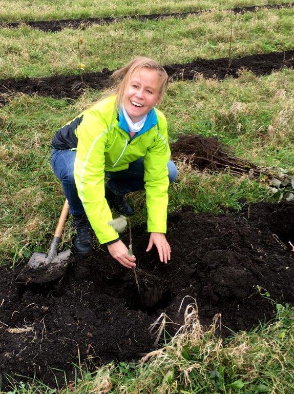 Irene Smetana planting a tree sitting on her haunches