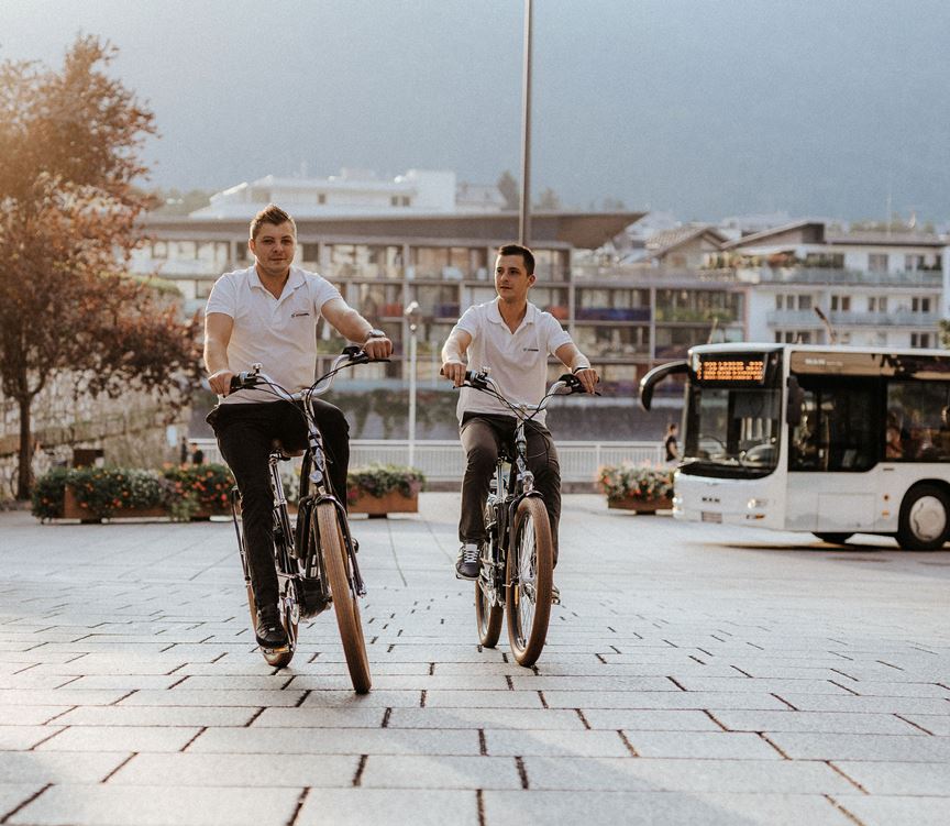 Two young men with e-bikes, apartments and bus in the back